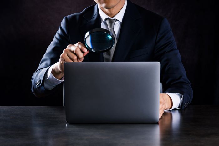 虫眼鏡でPCを見る男性